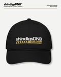A black baseball cap with 'shindigsDNB clothing' printed on the front in white and yellow, shown against a light gray background with brand text at the top.