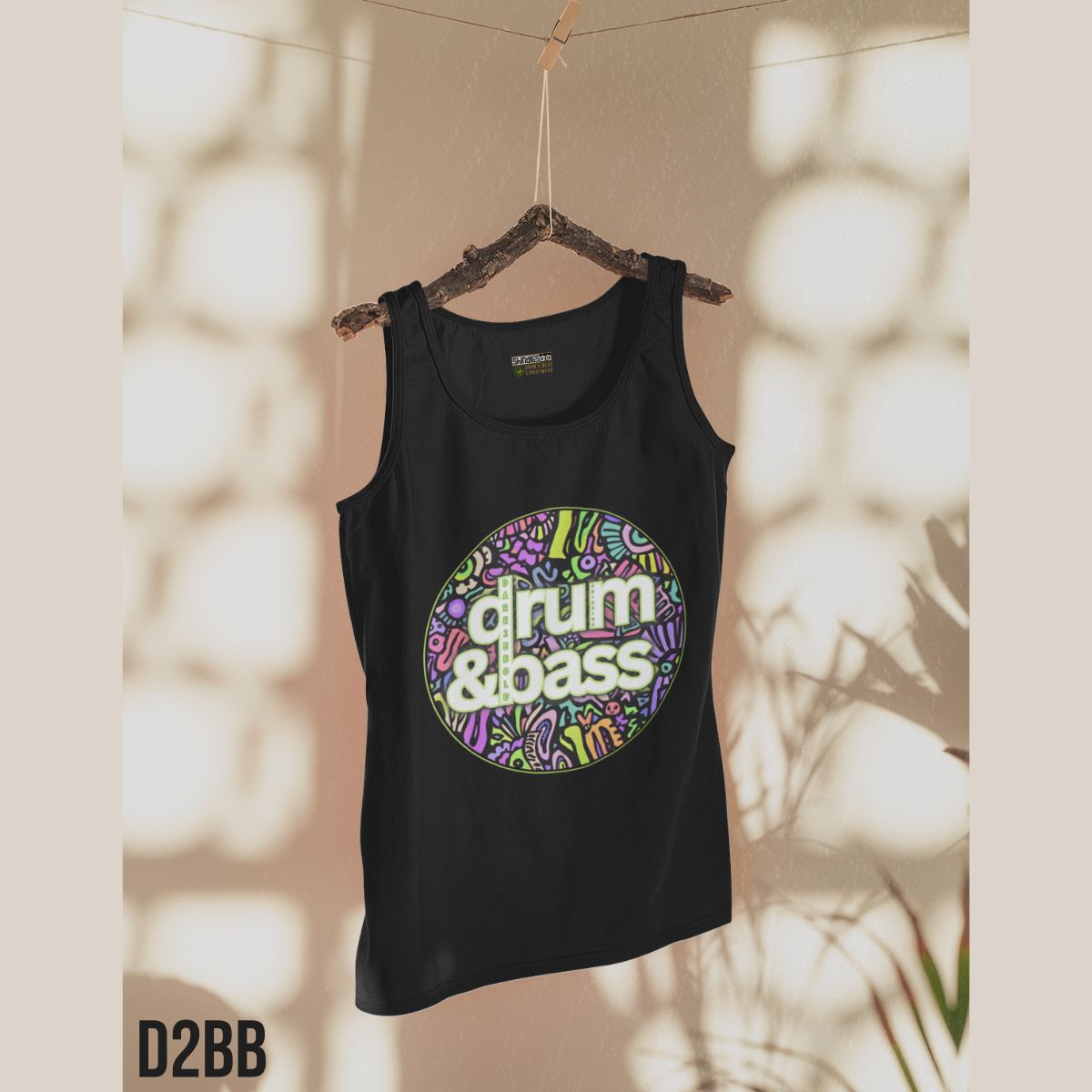 Black tank top with 'drum & bass' design on a hanger against a textured wall.