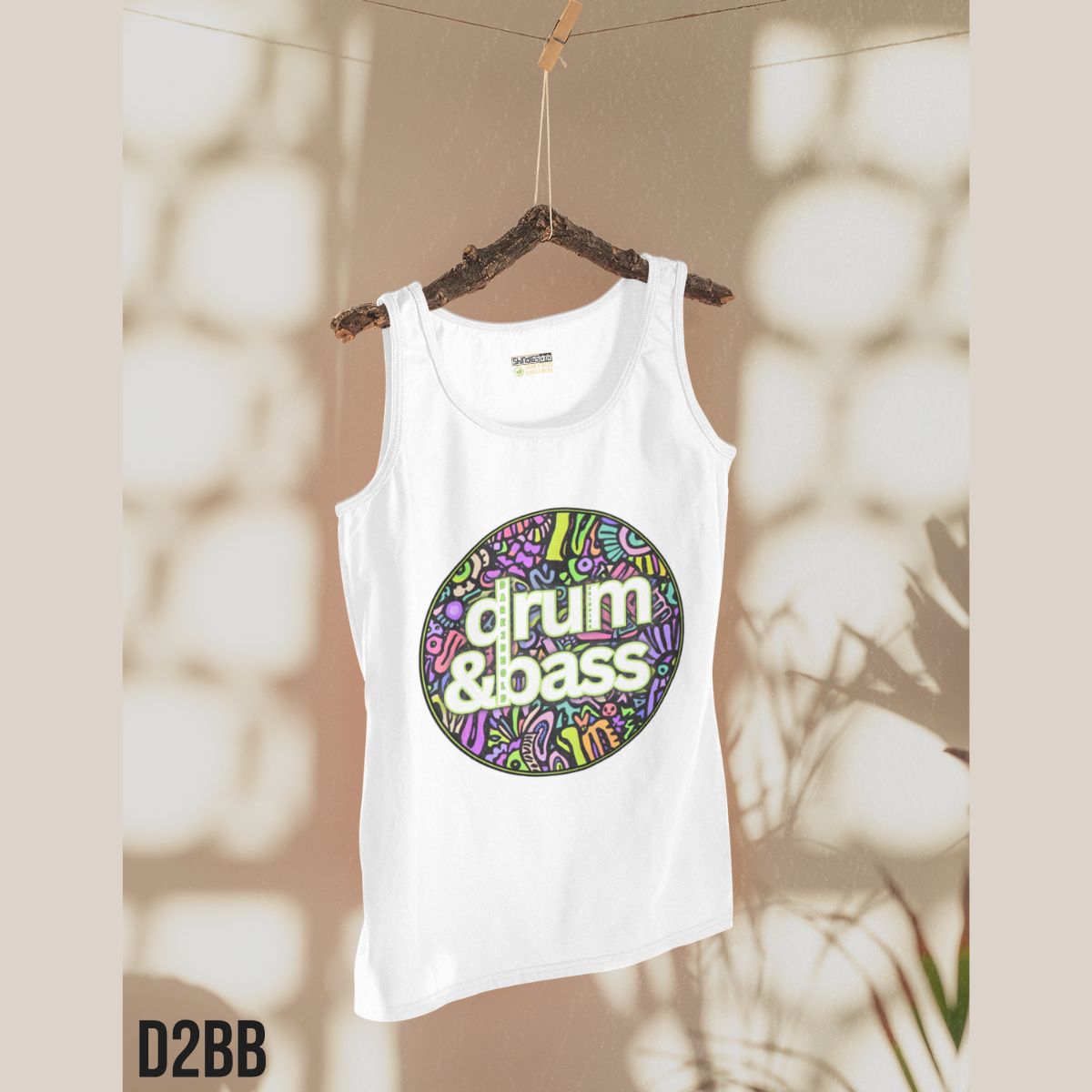 White tank top with 'drum & bass' design on a hanger against a blurred natural background