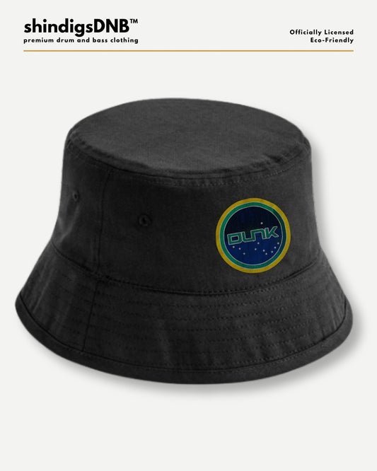 A black bucket hat with a circular embroidered patch featuring the word 'CUNK' in green on a blue background with a yellow border, shown on a light gray background with branding text at the top.