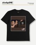 A black short-sleeve t-shirt with a square graphic print on the front, featuring an illustration of two women and a zombie, with the text 'Zombie Girls' in a stylized font. The shirt is displayed flat against a light gray background with branding text for 'shindigsDNB' at the top.