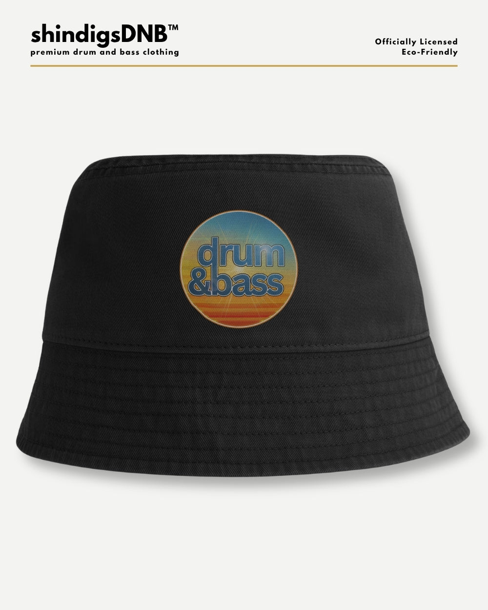 A black bucket hat with a circular retro-style graphic on the front featuring the words 'drum & bass' in blue over a yellow, orange, and blue sunset gradient. The hat is displayed against a light gray background with branding text at the top.